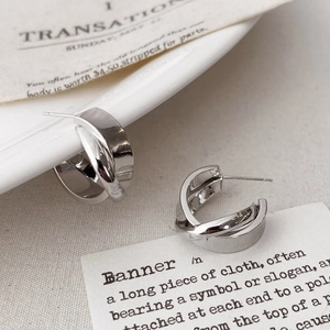 Detail shot of silver C-shaped twisted knot earrings on a vintage paper background