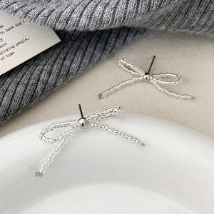 Detail of silver beaded bow earrings on a white plate with elegant knit background