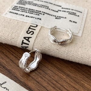 Detail of silver wavy huggie earrings with beaded edges on a rustic wood surface