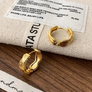 Close-up of golden wave textured hoop earrings with beaded edges on a rustic background