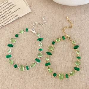 Elegant gold and silver bracelets featuring various green zircon shapes on rustic linen background