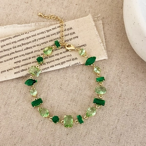 Detail of gold bracelet with irregular emerald green crystals on a beige fabric background