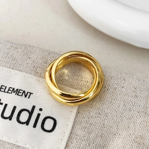 Detailed view of a gold-tone triple interlocking band ring on neutral fabric background