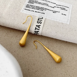 Detail of matte gold teardrop earrings with brushed metal finish on beige fiber texture