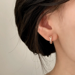 Gros plan de boucles d'oreilles créoles entrelacées en or rose serties de zircons brillants