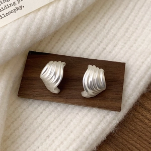 Close-up of matte silver seashell stud earrings with pleated texture on dark wood