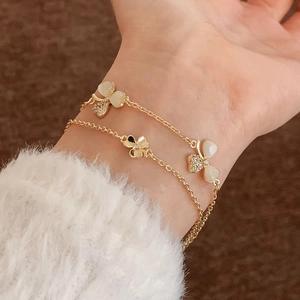 Double-layered 18K gold bracelet with clover motifs and zircon inlays on a white sweater