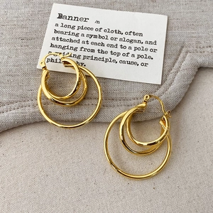 Detailed view of layered gold hoop earrings with three interlocking rings on linen cloth