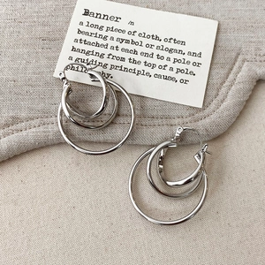Detail view of silver multi-layered concentric hoop earrings on a textured linen fabric