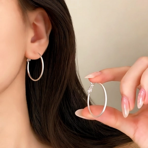 Close-up of minimalist silver hoop earrings worn on ear and held by hand showing closure