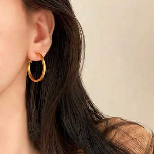 Close-up of a model wearing large matte gold geometric hoop earrings with a brushed finish