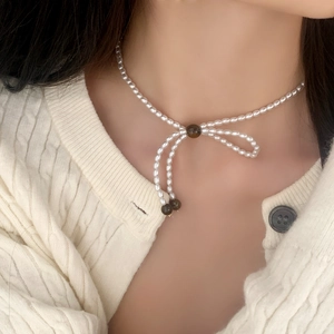Collier élégant en perles avec nœud et accents de pierres sombres sur cardigan blanc