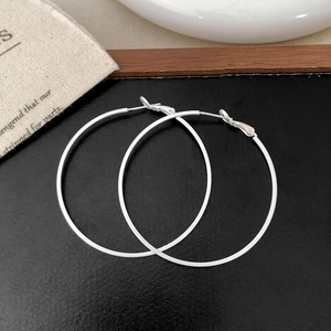 Close-up of minimalist large hoop earrings with secure clasp on a rustic textured background