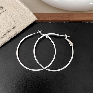 Detail of classic large silver hoop earrings with matte finish on textured black surface