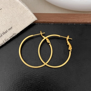 Detailed view of large gold hoop earrings with secure clasp on textured black background