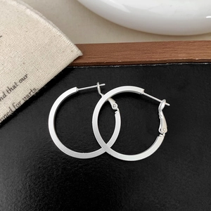 Close-up of matte silver geometric hoop earrings with secure clasp on a natural linen bag