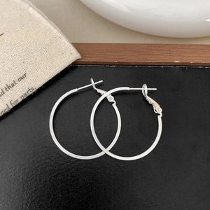 Detail shot of silver round hoop earrings on dark background with minimalist props