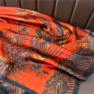 Detail of silk scarf showing vibrant orange phoenix pattern and smooth satin texture