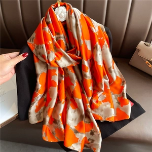 Artistic silk shawl with bright orange and beige abstract patterns on a leather sofa