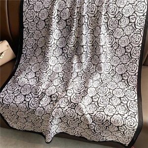 Luxurious long silk scarf with black and white rose pattern draped on a leather sofa