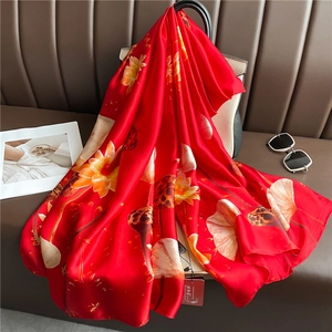 Close-up of red silk scarf with lotus print draped over a luxury handbag on a leather sofa