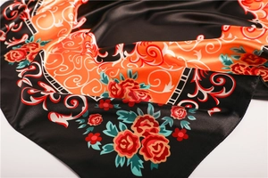 Détail d'un foulard en satin aux motifs floraux orange et vert sur soie noire