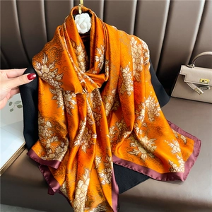 Detail of silk scarf with orange-gold floral patterns and burgundy borders on leather