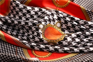 Detail of silk-like houndstooth scarf with orange color blocking and gold emblem patterns