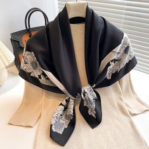 Detail of silk-textured black square scarf with white floral print on a beige knit top