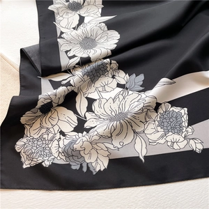 Close-up of black silk scarf with white floral print and elegant diagonal stripes