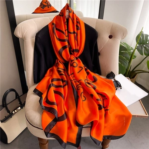 Orange silk scarf with black logo print draped on chair in luxury resort style