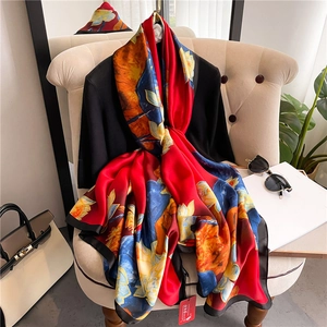 Macro shot of large silk scarf featuring red floral patterns draped over beige furniture
