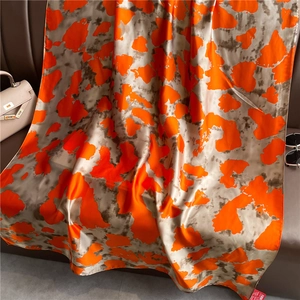 Luxury ink wash silk scarf in orange and grey draped over a leather surface