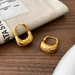 Detail of golden U-shaped earrings with hammered texture on a rustic wooden surface