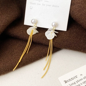 Élégantes boucles d'oreilles dorées à glands avec perles et disques de coquillage sur carte