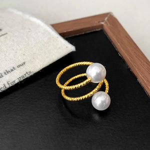 Detailed view of gold plated twisted ring band featuring two white pearls on black surface