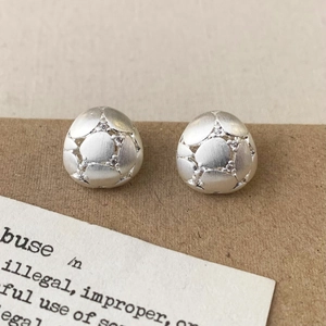 Macro view of matte silver stud earrings with brushed texture and micro-set zircon accents