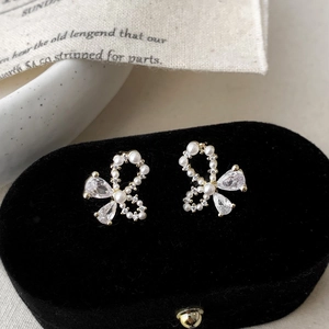 Detail of elegant gold bow earrings with white pearls and sparkling teardrop zircons