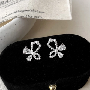 Detail of bow-shaped stud earrings with white pearls and sparkling teardrop zircons