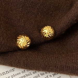 Macro shot of gold-plated circular stud earrings with elegant spiral textured pattern