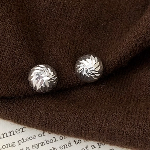 Macro shot of silver circular stud earrings with radiant faceted texture on knit fabric