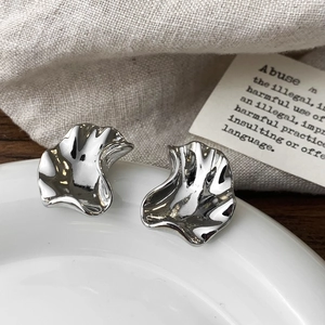 Detailed view of silver irregular crumpled stud earrings on white ceramic plate