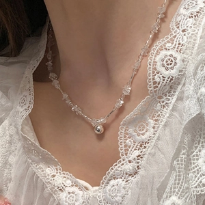 Elegant clear glass bead necklace with a polished silver ball pendant on a lace blouse