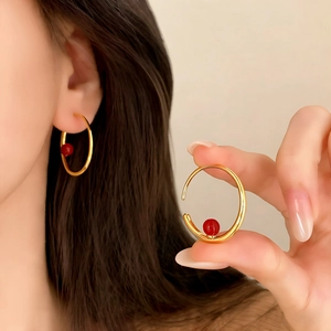 Boucles d'oreilles créoles dorées avec perle rouge montrées portées et en gros plan