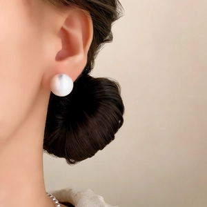 Close-up of large round white pearl stud earring worn by model with elegant luster