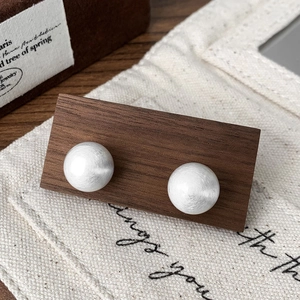 Detail of silver brushed matte semi-sphere stud earrings on dark walnut wood display