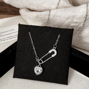Détail de collier trombone argenté avec pendentif en forme de cœur et zircons incrustés
