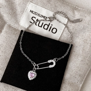 Détail de bracelet en argent avec trombone en zircon et breloques cœur rose sur fond de lin