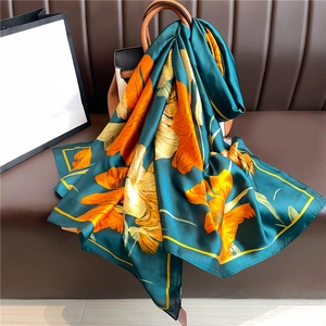 Détail d'un foulard en soie vert à motifs floraux oranges drapé sur un sac en cuir