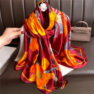 Détail d'un long châle soyeux aux motifs floraux éclatants sur un tissu rouge profond